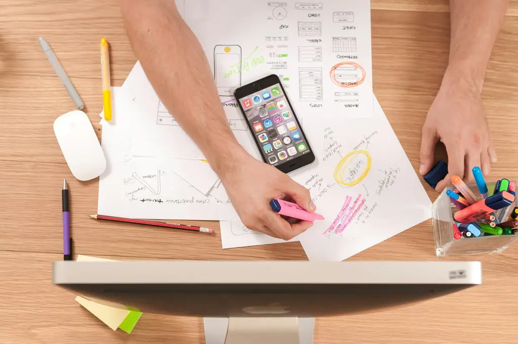 Hands sketching mobile app wireframes on paper next to a smartphone
